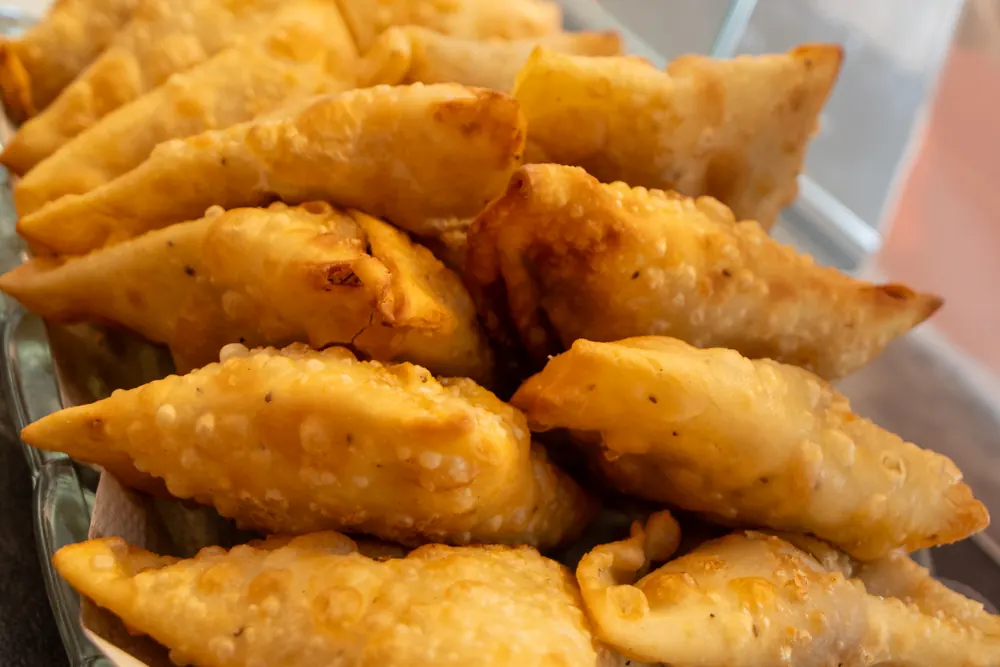 Frisch frittierte Samosa, goldbraune Teigtaschen auf einem Blech an der Theke.
